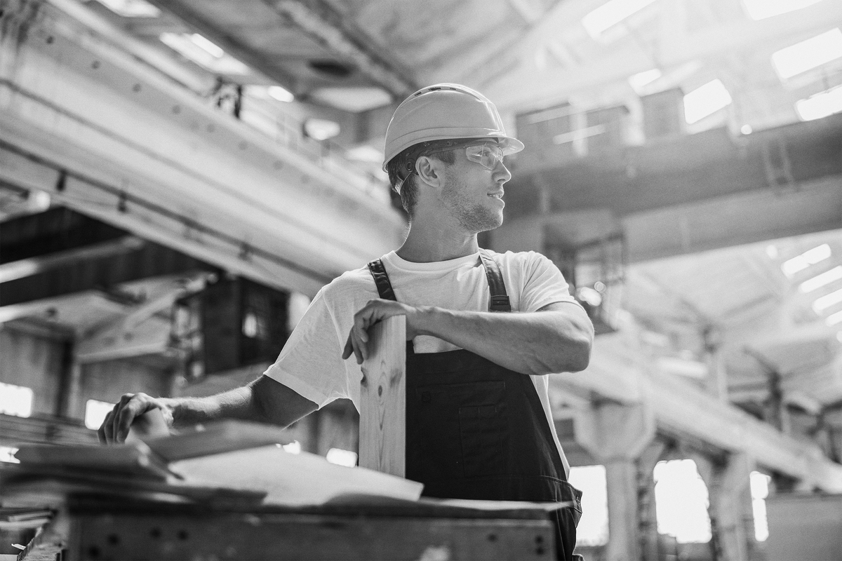 Mand i sikkerhedshjelm og briller holder et bræt i et værksted